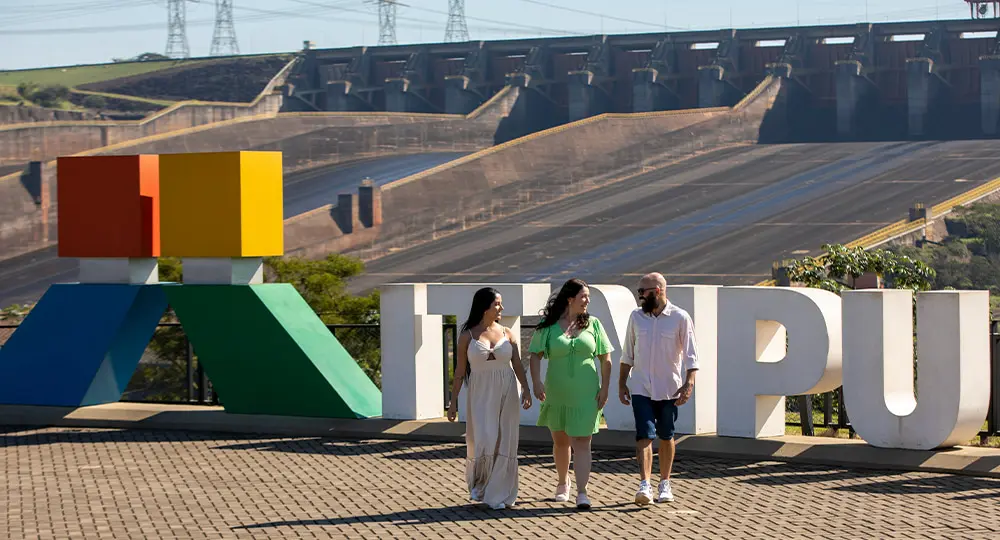 Three people, two women and one man, walking at the Spillway Viewpoint of the Itaipu Hydroelectric Plant, in Foz do Iguaçu.